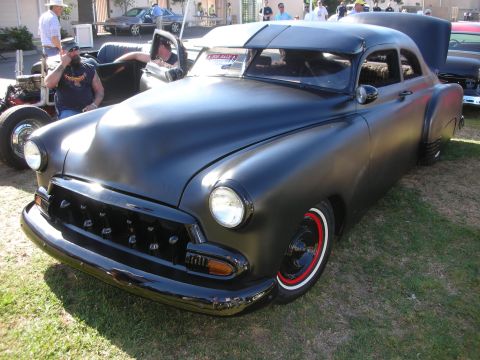 1998 Ford Crown Victoria - matte black chopped custom coupe with whitewall tires and a Chevrolet-style grille sits on grass at an outdoor car show.