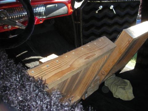 1998 Ford Crown Victoria - interior of a custom car shows rough wooden boards laid over purple shag carpet beside a red dash and chrome steering wheel.