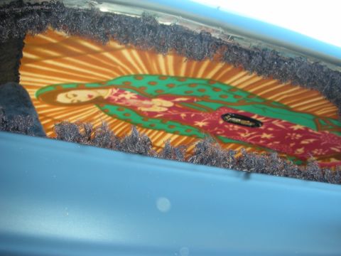 1998 Ford Crown Victoria - colorful Virgin of Guadalupe graphic glimpsed through a frayed weatherstrip opening on a light blue vehicle panel.