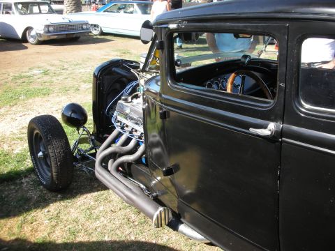 1998 Ford Crown Victoria - black chopped hot rod showing its exposed front axle, polished engine and lakester-style side exhaust, parked on grass at a show.