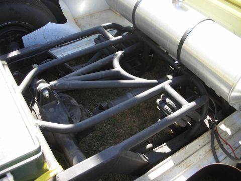 1998 Ford Crown Victoria - Detail of a black tubular four-link rear suspension and polished tank beneath the bed of a yellow custom truck.