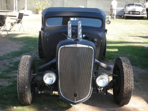 1998 Ford Crown Victoria - Head-on view of a black channeled hot rod truck with tall chrome grille, twin velocity stacks and an exposed dropped front axle on wide tir…