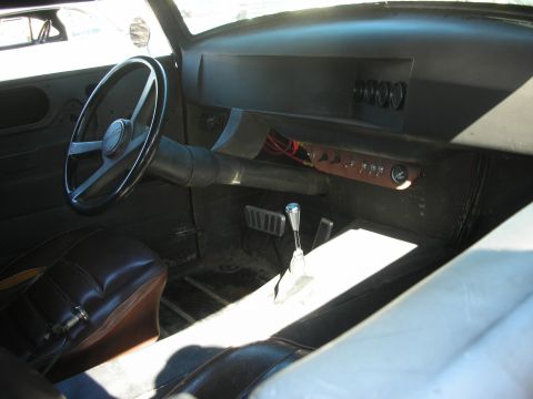 1998 Ford Crown Victoria - bare-bones custom interior showing a black steering wheel, simple dash with gauges, bench seat and a tall chrome shifter through the floor.