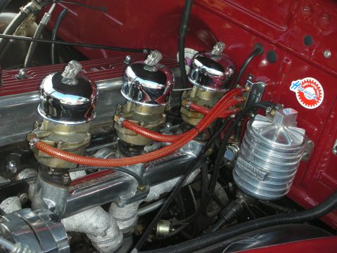 1998 Ford Crown Victoria - Close-up of a triple-carburetor setup with chrome air cleaners and red braided fuel lines in a deep-red engine bay.