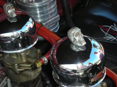1998 Ford Crown Victoria - pair of polished carburetor air cleaners crowned with chrome skull ornaments and wrapped in red braided lines, reflecting the sky.