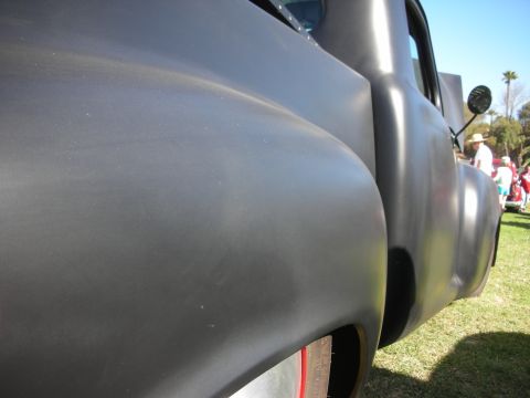 1998 Ford Crown Victoria - Tight detail of a satin-gray custom's smooth rear fender, body line and door with a small round mirror, blue sky and grass beyond.
