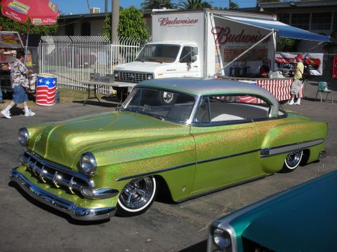 1998 Ford Crown Victoria - heavily lowered 1950s two-door coupe in shimmering green metalflake paint and whitewall tires parked at an outdoor show near a Budweiser tr…
