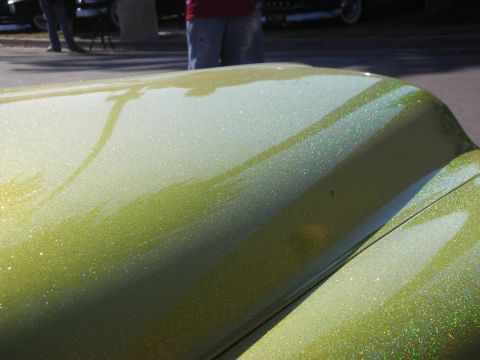 1998 Ford Crown Victoria - Extreme close-up of glittering green metalflake paint reflecting sunlight across the curved body panels of a custom car.