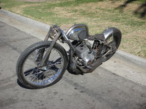 1998 Ford Crown Victoria - stripped, bare-metal rigid bobber motorcycle with a peanut tank and exposed engine sits parked along a street curb.