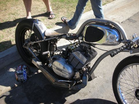 1998 Ford Crown Victoria - custom bare-metal chopper with a vertical twin engine and a 'Dirty Max' tank parked at a curb as a person steps past.