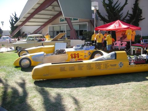 1998 Ford Crown Victoria - yellow belly-tank-style streamliner racer numbered 131 sits on grass at a car show with crew members in matching yellow shirts.