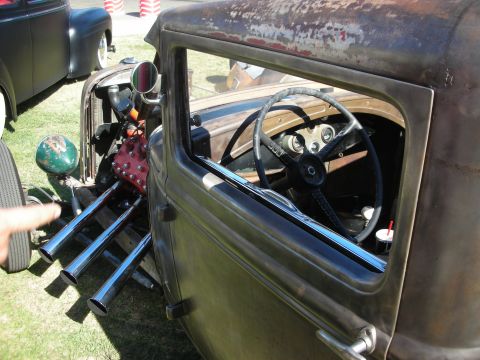 1998 Ford Crown Victoria - View into the open cockpit of a patina rat rod showing a wood-rim steering wheel, simple dash and the red flathead engine ahead.