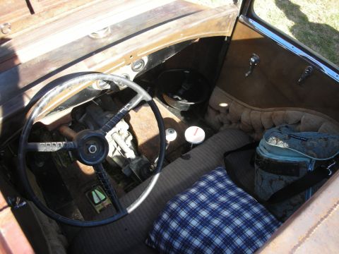 1998 Ford Crown Victoria - Spartan interior of an old vehicle showing a large dark steering wheel, a small gauge, plaid blanket and worn upholstery.