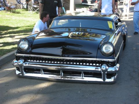 1998 Ford Crown Victoria - Front view of a glossy black chopped custom car with a heavy chrome split bumper and frenched headlights at an outdoor show.