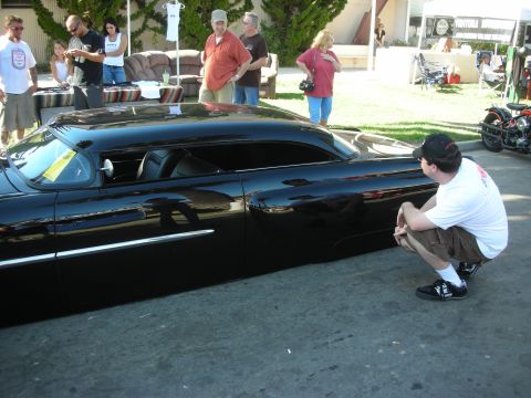 1998 Ford Crown Victoria - Side view of a low glossy black chopped custom coupe with a chrome side spear as a man crouches beside it.