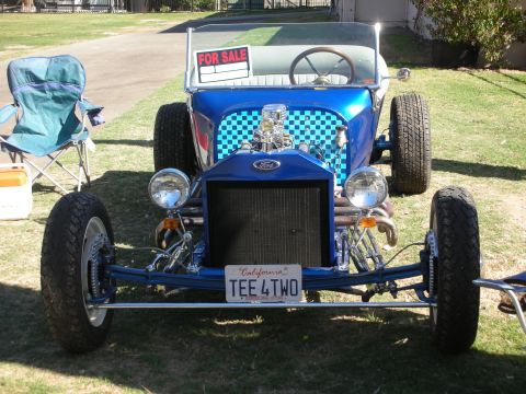1998 Ford Crown Victoria - blue Ford T-bucket hot rod roadster with checkered fenders, a FOR SALE sign and a California TEE 4 TWO plate parked on grass.
