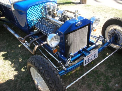 1998 Ford Crown Victoria - Close view of a blue T-bucket hot rod's chromed V8 engine, headers and radiator with a California TEE 4 TWO plate.