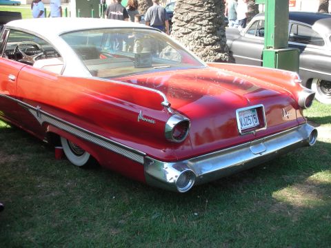 1998 Ford Crown Victoria - Rear-quarter view of a red finned 1960 Dodge Phoenix hardtop with a white roof and chrome bumper on grass.
