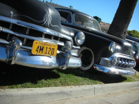 1998 Ford Crown Victoria - Close low view of two pinstriped black 1950s custom cars' front ends with a yellow 1947 California plate reading 4M 120.