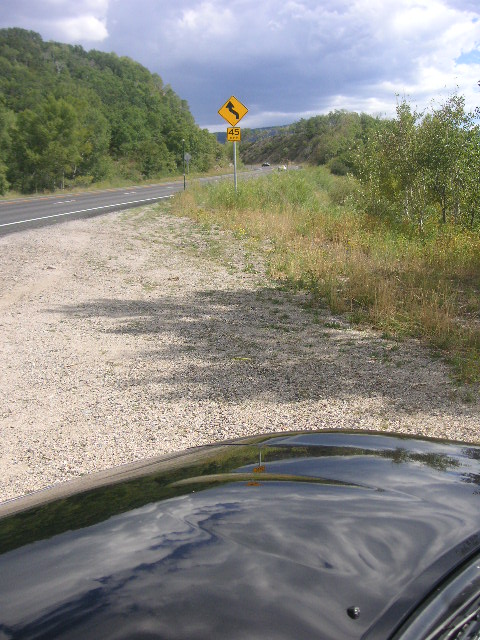 1996 Mazda Miata - A yellow curve warning sign is posted next to a highway on a cloudy day.