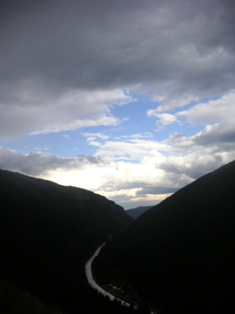1996 Mazda Miata - A scenic mountain valley features a winding road under a dramatic sky with clouds.