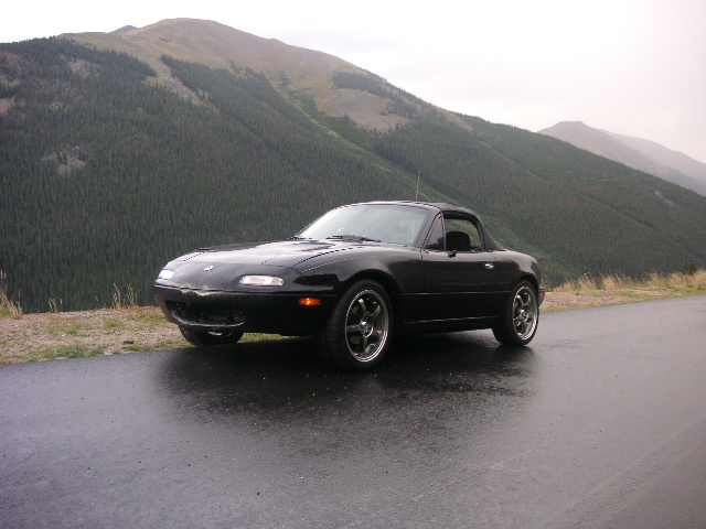 Black convertible sports car parked on a wet road with mountains in the background