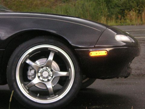 1996 Mazda Miata - Close-up view of a black car's front fender and wheel, aftermarket rims and an amber turn signal.