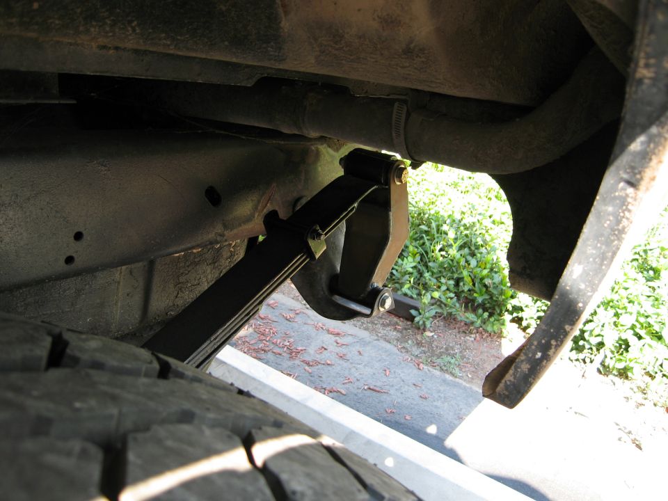 Underbody view of rear leaf spring with new black extended shackle and gold bolts