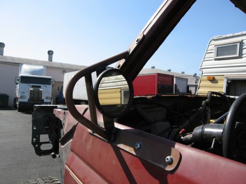 1986 Ford Bronco - The interior of a modified vehicle shows a roll cage and a side mirror, with other vehicles parked in the lot.