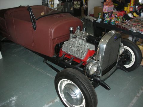 1998 Ford Crown Victoria - maroon highboy roadster hot rod with a chromed flathead V8 and whitewall tires sits indoors near a toy display.