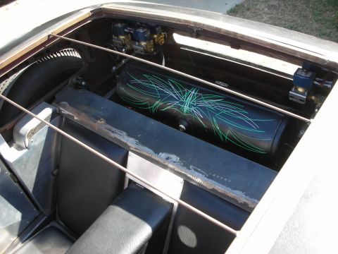1998 Ford Crown Victoria - black cylindrical tank with green pinstriping sits behind the bench seats in the open rear compartment of a hot rod.