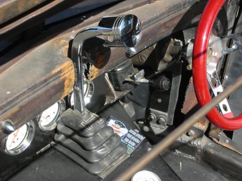1998 Ford Crown Victoria - Close view of a hot rod cabin showing a chrome floor shifter, round gauges and a red steering wheel against weathered bodywork.