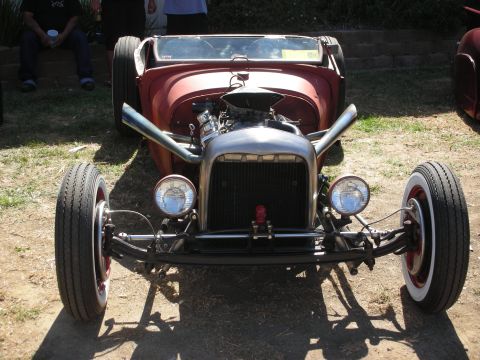 1998 Ford Crown Victoria - Head-on view of a silver bare-metal hot rod roadster with a chrome blower, headers and whitewall tires over a red body.
