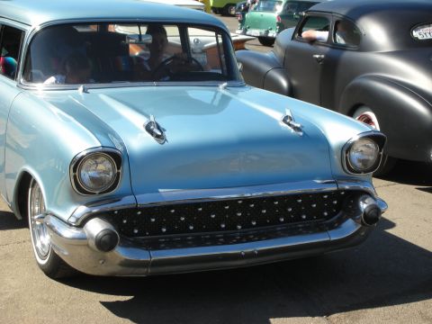 1998 Ford Crown Victoria - Front three-quarter view of a light blue 1957 Chevrolet sedan with bullet bumper guards and a custom mesh grille.