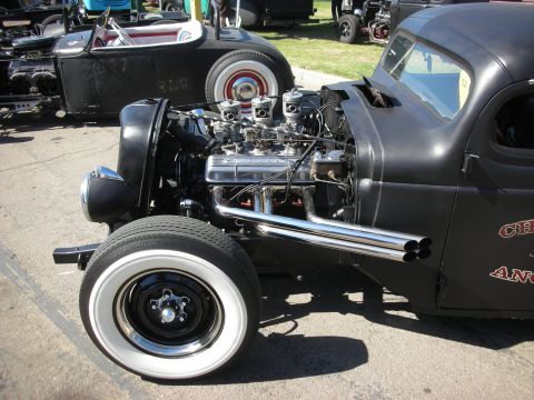 1998 Ford Crown Victoria - Side view of a black rat rod showing its exposed chrome multi-carb V8, side-exit headers and a whitewall on a steel wheel.