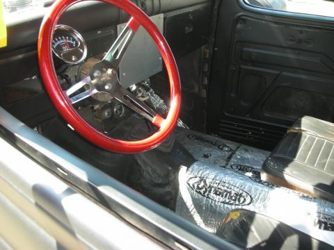 1998 Ford Crown Victoria - Stripped hot rod cabin showing a red steering wheel, single round gauge and silver heat-shield insulation on the floor.