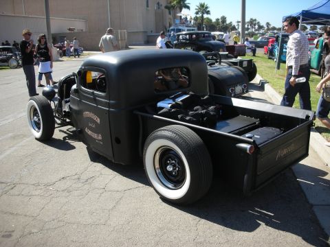 1998 Ford Crown Victoria - flat-black chopped rat rod pickup with whitewall tires and an empty bed parked on pavement among onlookers at a show.