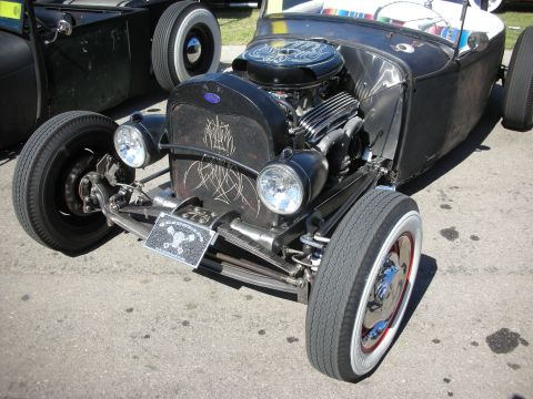 1998 Ford Crown Victoria - Front of a black hot rod roadster with white pinstriping, exposed engine, twin headlights and a skull-themed grille plate.