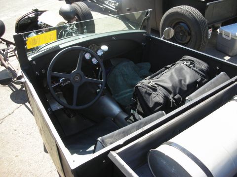 1998 Ford Crown Victoria - Interior of an open hot rod roadster showing a black four-spoke steering wheel, bare cockpit and a black duffel bag on the seat.