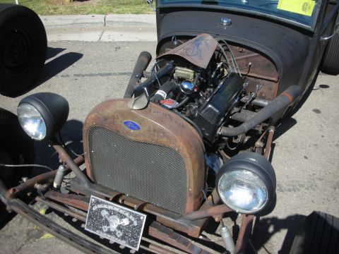 1998 Ford Crown Victoria - Front of a bare-metal rat rod with a rusty Ford grille shell, twin headlights and an exposed engine at a show.