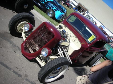 1998 Ford Crown Victoria - maroon-and-cream channeled hot rod with an exposed engine, dropped front axle and tall rear tires at an outdoor show.