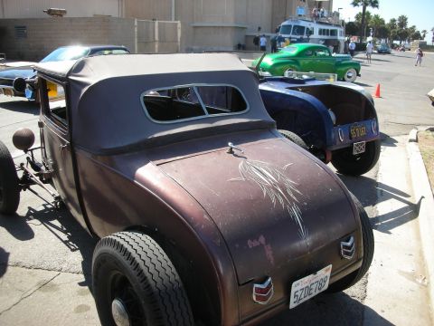 1998 Ford Crown Victoria - Rear quarter of a brown patina chopped hot rod roadster with pinstriping and a California plate, a green coupe behind it.