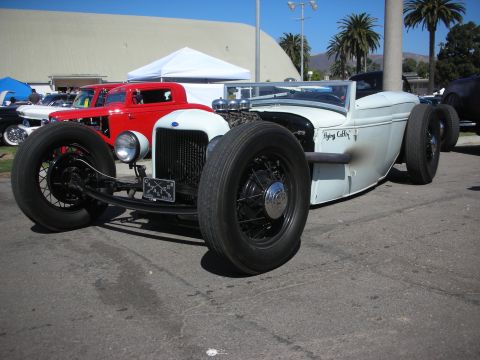 1998 Ford Crown Victoria - white low-slung hot rod roadster with exposed engine, wire wheels and Flying Coffin lettering parked at an outdoor show.