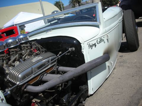1998 Ford Crown Victoria - Close view of a white hot rod's exposed engine with finned valve covers, headers and Flying Coffin script on the cowl.