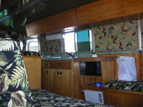 1998 Ford Crown Victoria - Interior of a vintage camper with wood paneling, retro bird-print curtains and tropical-leaf upholstered seating.