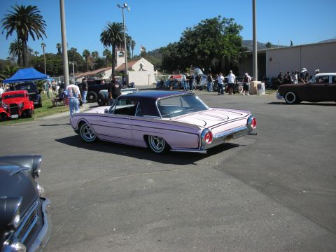 1998 Ford Crown Victoria - pink lowered Ford Thunderbird hardtop coupe parked on pavement with hot rods and spectators behind at a show.