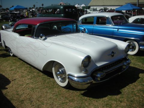 1998 Ford Crown Victoria - lowered white 1950s Oldsmobile hardtop with a red roof and subtle ghost flames sits on whitewall tires among classic cars at an outdoor sho…