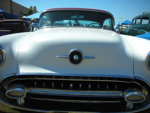 1998 Ford Crown Victoria - Close front view of a white 1950s Oldsmobile with chrome bullet bumper and OLDSMOBILE lettering across the grille under a clear blue sky.
