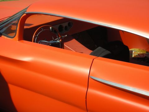 1998 Ford Crown Victoria - Close side view through the window of an orange custom car revealing a chrome steering wheel and round gauges in the dash.