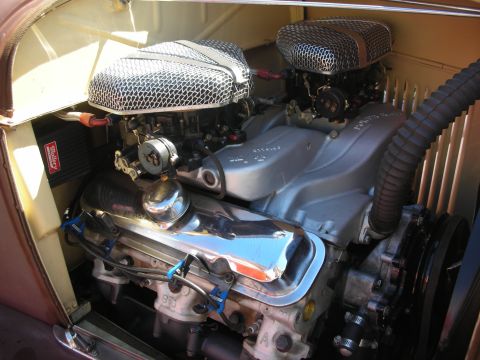 1998 Ford Crown Victoria - twin-carburetor V8 hot rod engine with mesh velocity-stack air cleaners and a chrome valve cover sits in an engine bay at a show.